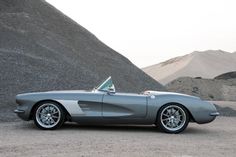 a silver sports car is parked in front of some hills and sand dunes on a cloudy day