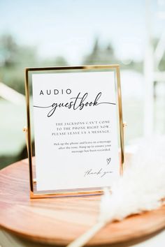 a wedding guest book is sitting on a wooden table with a white feather in front of it