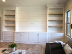 an empty living room with white cabinets and wood flooring on the walls, in front of a fireplace