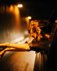 a woman leaning on the side of a car at night with her head in her hands