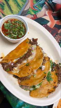 a white plate topped with three tacos next to a bowl of salsa and sauce