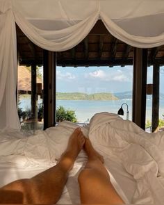 a man laying in bed with his feet up on the edge of the bed and looking out over the water