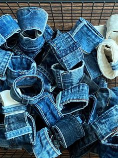 several pairs of blue jeans sitting in a wire basket next to rolled up toilet paper