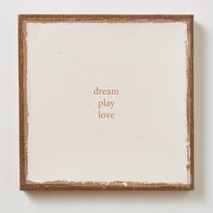 a square wooden frame with the words dream play love on it in red ink against a white background