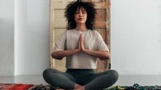 a woman sitting in a yoga pose with her eyes closed and hands folded up to the side