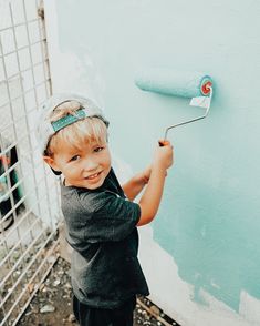 a young boy painting the side of a blue wall