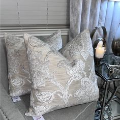 two pillows sitting on top of a couch next to a table with candles and vases