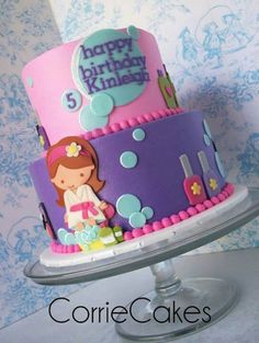 a three tiered birthday cake decorated with pink and purple icing, featuring a girl on top