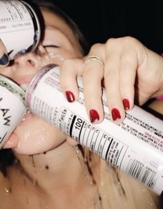 a woman with red nails is drinking from a white bottle while she's covered in water