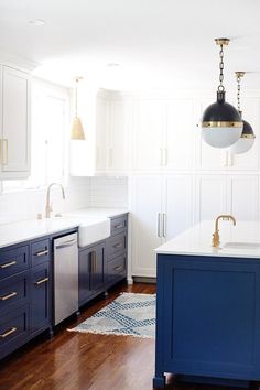 a kitchen with white cabinets and blue island in front of the sink, lights hanging from the ceiling