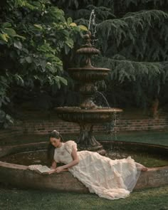 a woman in a white dress sitting on a stone wall next to a water fountain