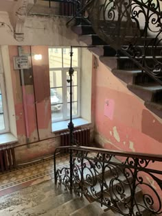 an old staircase with wrought iron handrails and pink paint on the wall behind it