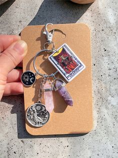 a hand holding a keychain with charms attached to it on top of a piece of cardboard