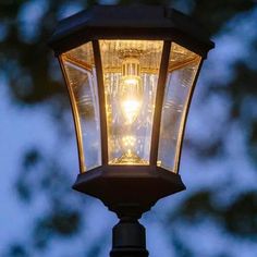 an old fashioned street light lit up in the night sky with trees in the background