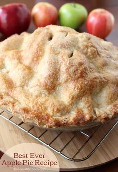 an apple pie on a cooling rack with apples in the background