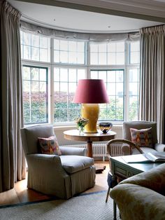 a living room with two chairs and a lamp in the corner near a couch, coffee table and window