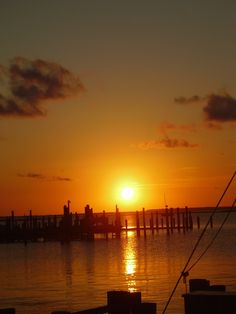 the sun is setting over the water and some docks are in the distance with clouds