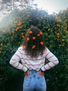 the back of a woman's head with flowers in her hair and jeans on