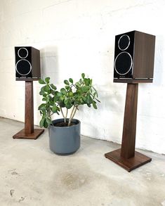 three wooden speakers sitting next to each other on top of a cement floor near a potted plant