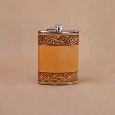 a leather flask with an intricate design on the front and side, sitting on a tan background