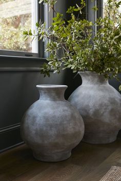 two gray vases sitting next to each other on a wooden floor in front of a window