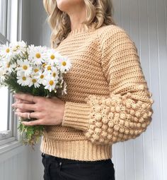 a woman holding a bouquet of daisies in front of a window