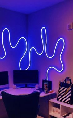 a desk with two computer monitors and a bag on top of it in front of a purple wall