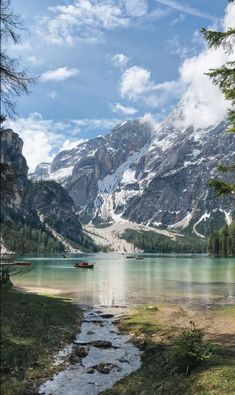 there is a boat that is in the water near mountains and grass on the shore