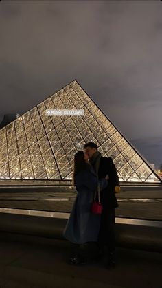 a man and woman standing in front of a building with a glass pyramid behind them