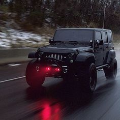 a black jeep driving down the road with red lights on it's front bumper