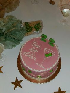 a pink birthday cake sitting on top of a table next to wine glasses and flowers