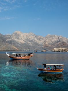 two boats floating on top of a body of water next to mountains in the background