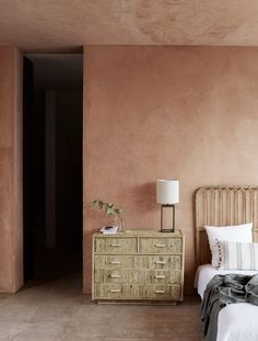 a bed sitting next to a wooden dresser in a bedroom under a pink painted wall