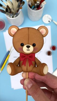 a hand holding a brown teddy bear on top of a wooden stick with a red bow