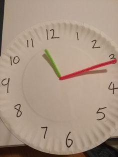 a paper plate with a green and red toothbrush on it next to a clock