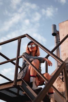 a woman sitting on top of a metal stair case next to a building with clouds in the background