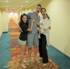 three people posing for the camera in an empty hotel hallway with blue carpet and yellow walls