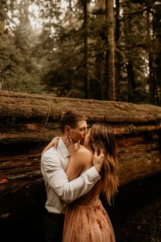 a man and woman kissing in front of a fallen tree at the bottom of a forest