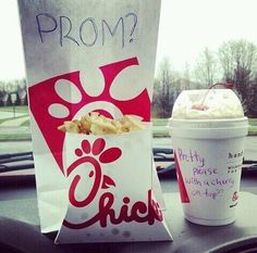 a cup of ice cream next to a paper bag with food in it on the dashboard of a car