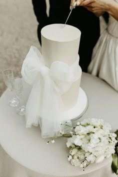 a bride and groom cutting into their wedding cake at the table with flowers on it