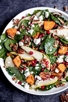 a white bowl filled with spinach, pears and feta cheese topped with pecans