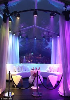 a stage set up for a party with purple lighting and white drapes on the ceiling