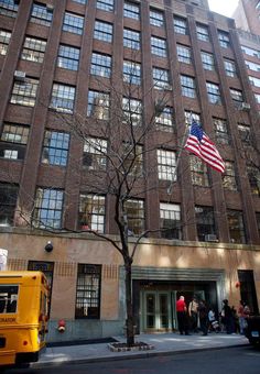 an american flag is flying in front of a large building with many windows and people walking on the sidewalk