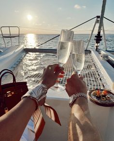 two people toasting with wine glasses on a boat in the ocean at sunset or sunrise