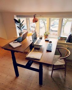 a wooden table topped with laptops next to a window filled with lots of windows