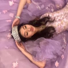 a woman laying on top of a bed wearing a purple dress and tiara with stars around her neck