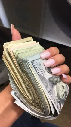 a woman's hand holding stacks of money in front of her face with pink nails