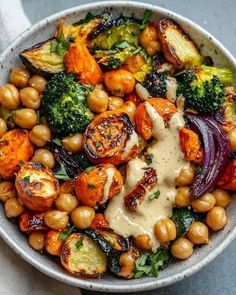 a bowl filled with broccoli, carrots and chickpeas covered in sauce