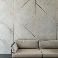 a couch sitting on top of a wooden floor next to a wall with geometric tiles