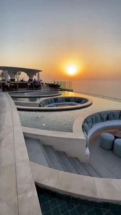 the sun is setting over an outdoor swimming pool with lounge chairs and tables around it